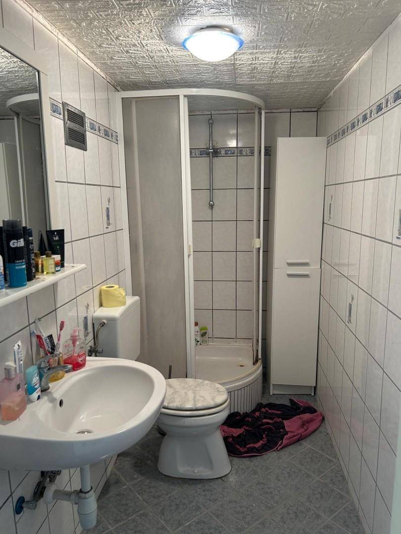 Kleines Badezimmer mit Duschkabine, WC, Waschbecken und weißen Fliesen.