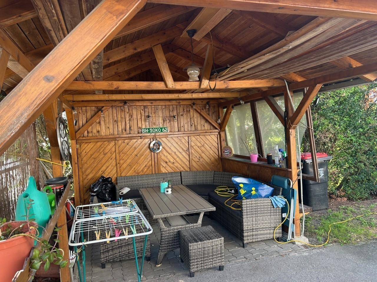 Gemütlicher überdachter Sitzbereich im Freien mit Rattanmöbeln und Holzwänden, ideal für gesellige Stunden.