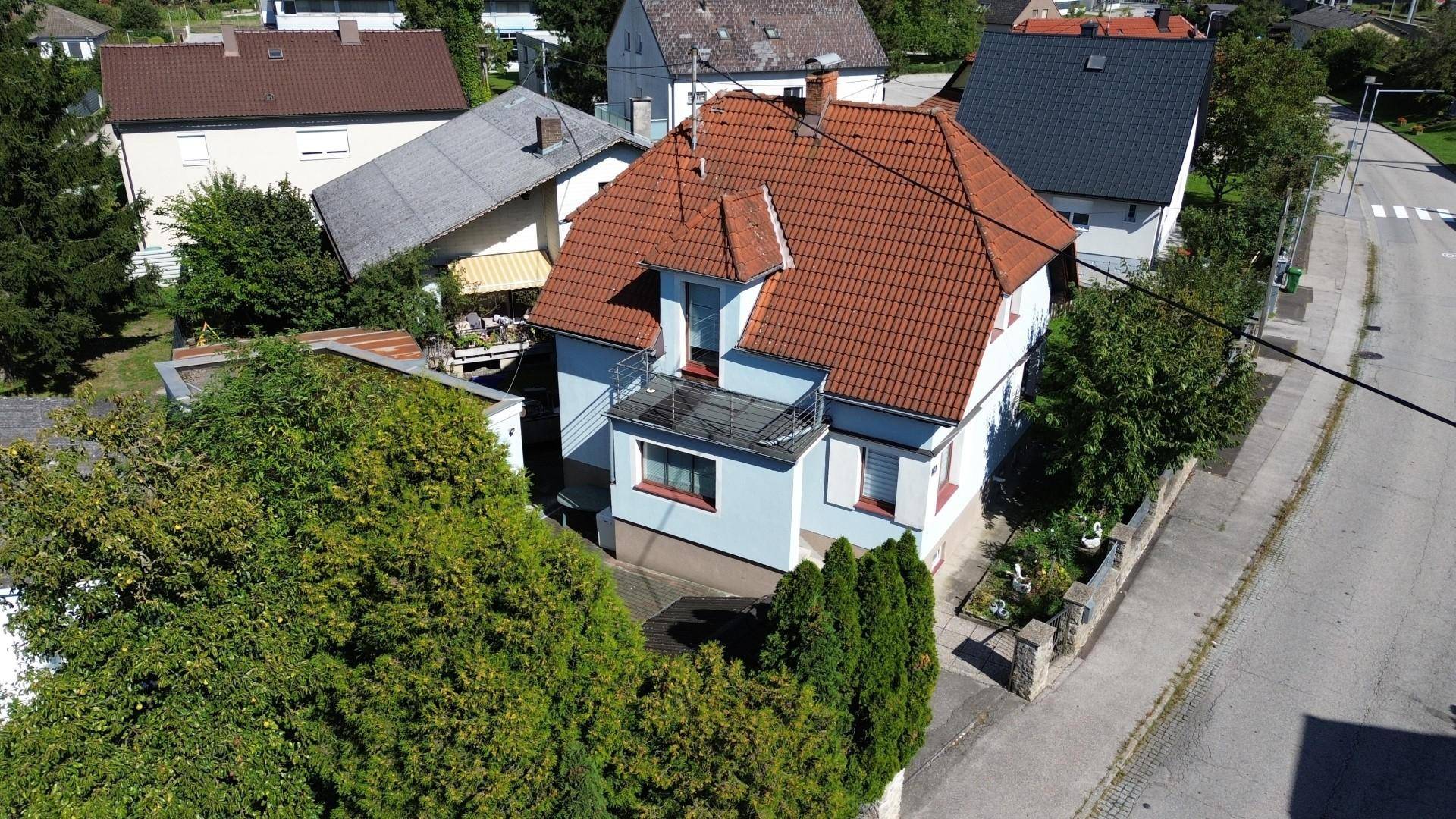 Luftaufnahme eines Wohnhauses mit rotem Ziegeldach, Balkon und umgebender grüner Vegetation.