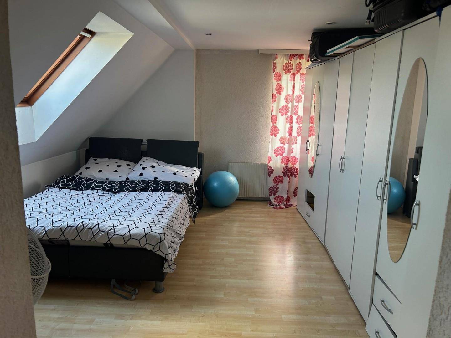 Helles Schlafzimmer im Dachgeschoss mit Bett, großem Kleiderschrank und Dachfenster.