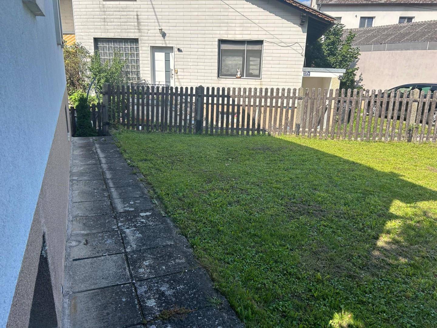 Grüner Gartenbereich mit Rasenfläche und Holzzaun hinter dem Haus.