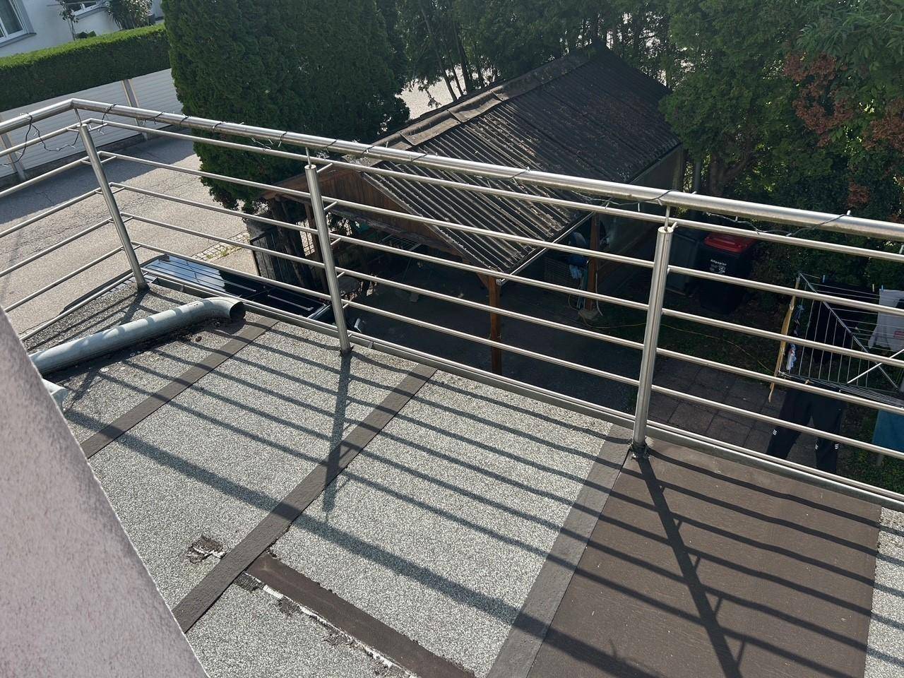 Balkon mit modernem Edelstahlgeländer und Blick auf den Carport und die grüne Umgebung.