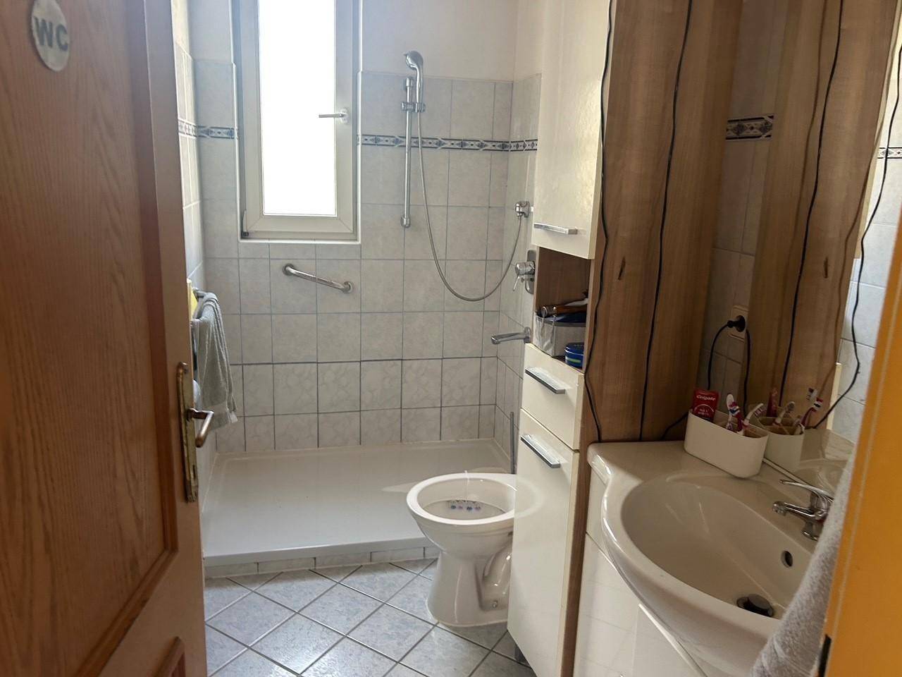 Badezimmer mit ebenerdiger Dusche, WC, Waschbecken und Haltegriffen für Barrierefreiheit.
