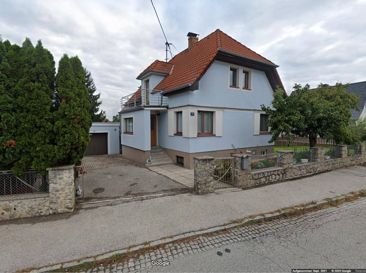 Einfamilienhaus mit hellblauer Fassade, rotem Ziegeldach und kleinem Balkon.