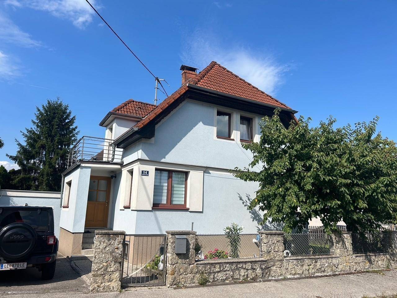 Vorderansicht eines Einfamilienhauses mit hellblauer Fassade, rotem Dach und kleinem Balkon.