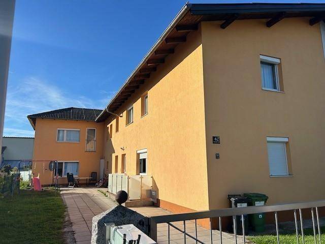 Seitenansicht des Gebäudes mit gelber Fassade, Hausnummer 42 und einem gepflasterten Zugangsbereich.