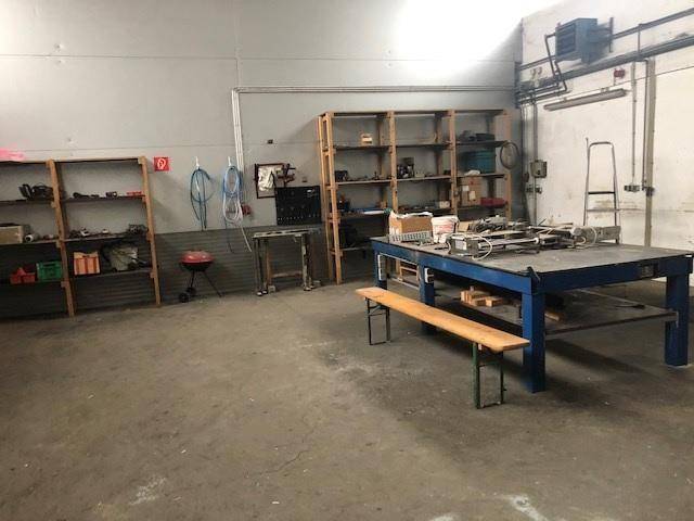 Geräumiger Werkstattbereich mit stabilen Regalen, einem großen Arbeitstisch und robustem Betonboden.