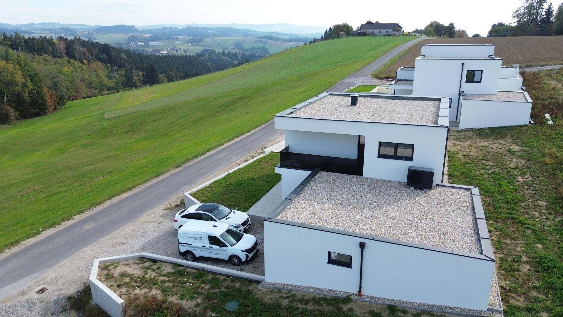 Mehrere moderne Neubauten mit Flachdächern in einer ländlichen Umgebung mit weitem Blick.