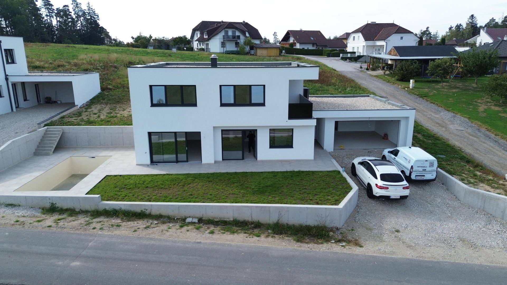 Modernes Einfamilienhaus mit leerem Poolbereich, Garten und Doppelgarage im Bau.