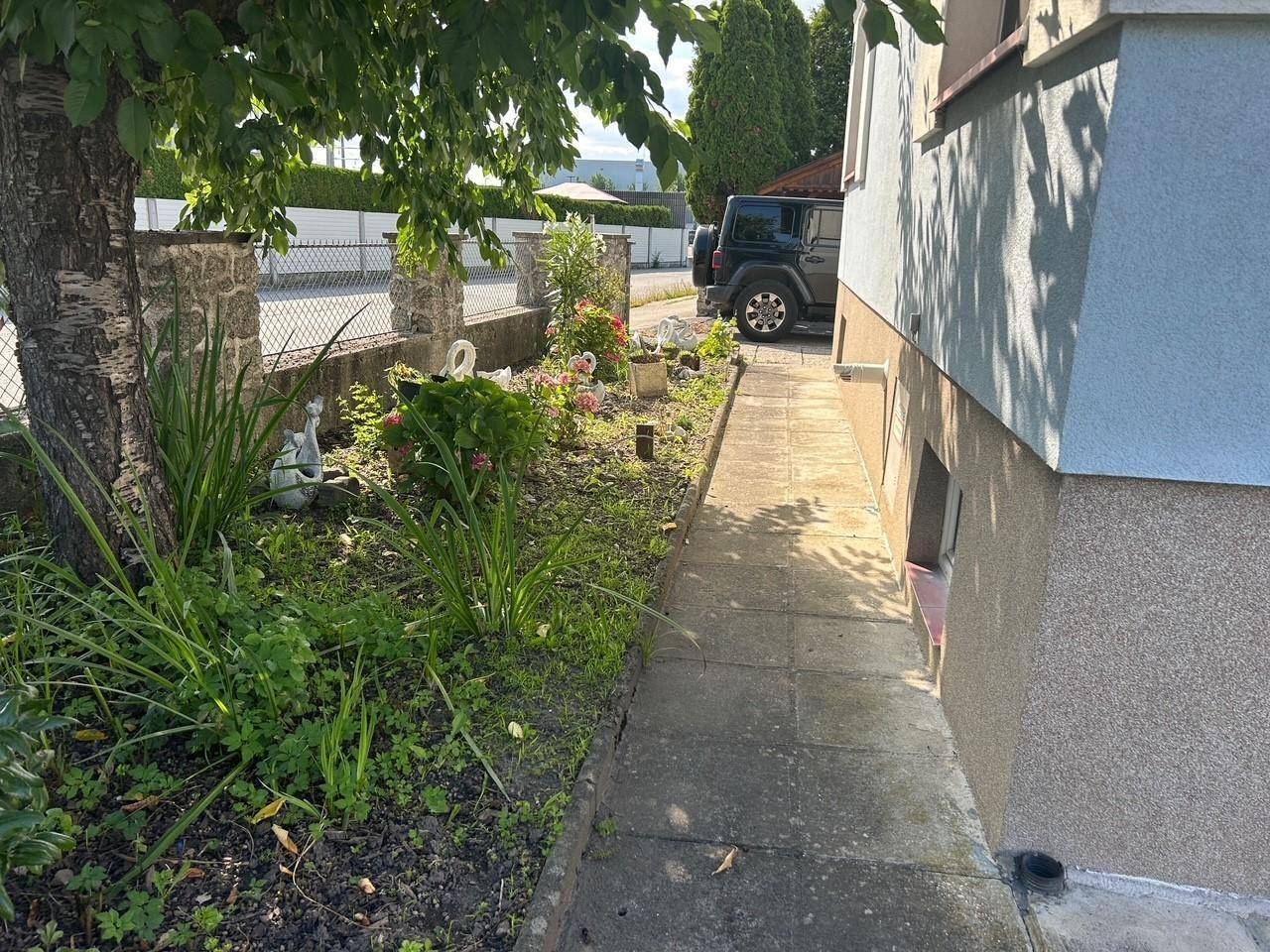 Kleiner Gartenweg entlang des Hauses mit Blumenbeeten und dekorativen Elementen.