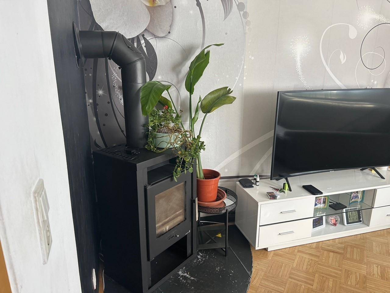 Wohnzimmer mit modernem Holzofen, Fernseher und dekorativer Tapete.