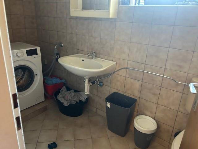 Gefliester Raum mit Waschmaschine, Waschbecken und Fenster, ideal als Hauswirtschaftsraum.