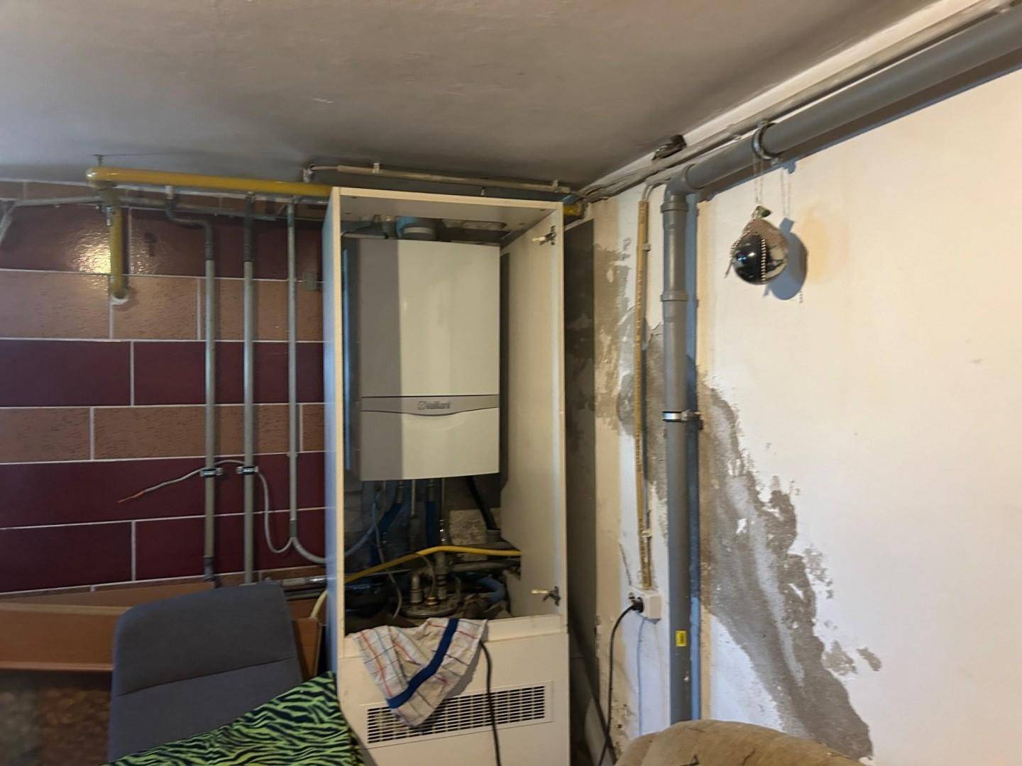 Raum mit Heizungsanlage und sichtbaren Rohren, der als Hauswirtschaftsraum dient.