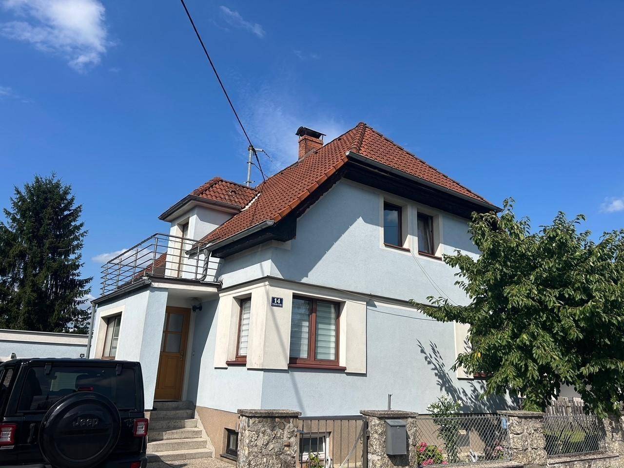 Ansicht des Einfamilienhauses mit hellblauer Fassade, braunen Fensterrahmen und kleinem Balkon.