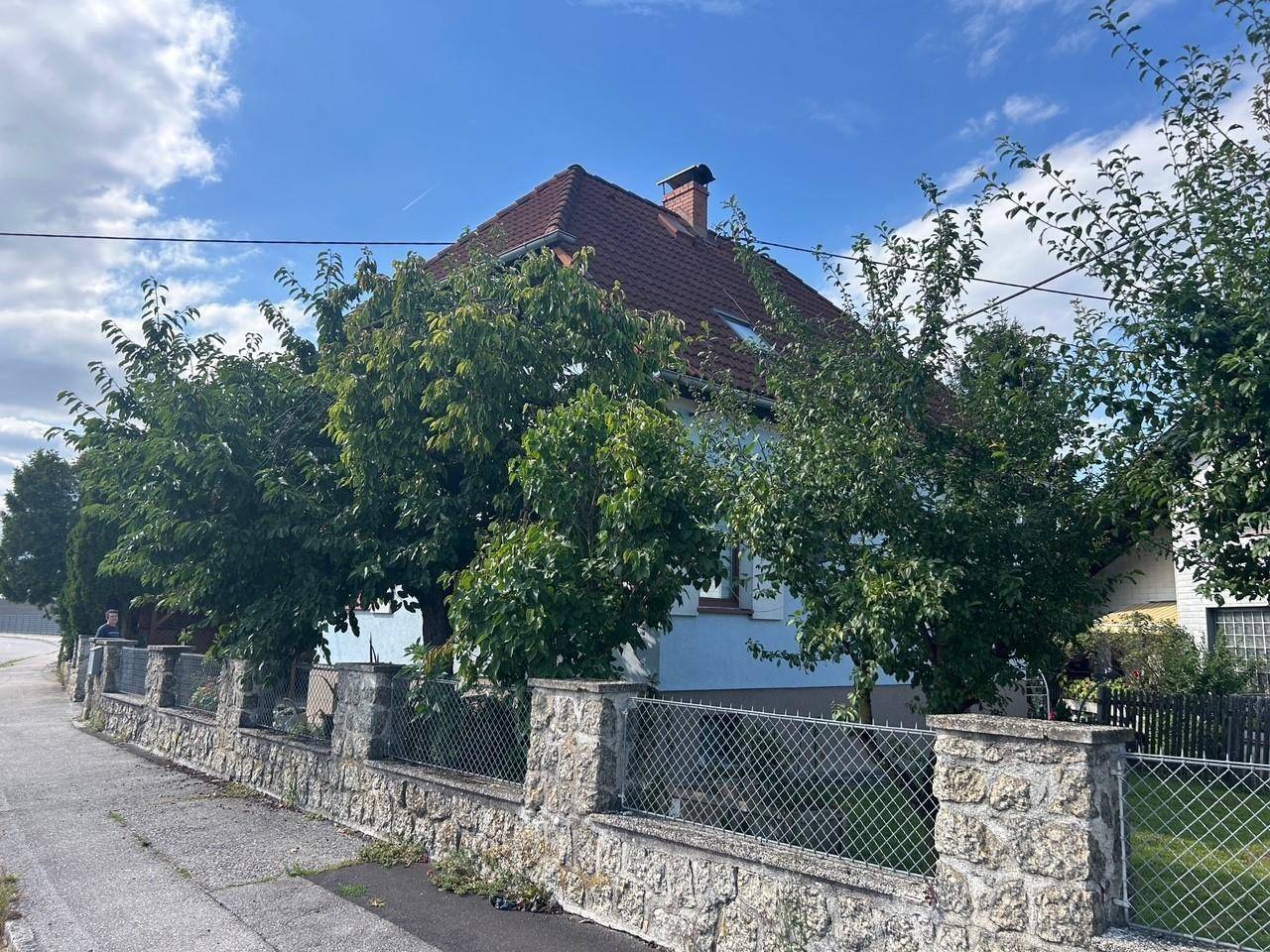 Seitenansicht des Hauses mit üppiger Bepflanzung und einem traditionellen Steinzaun im Vordergrund.