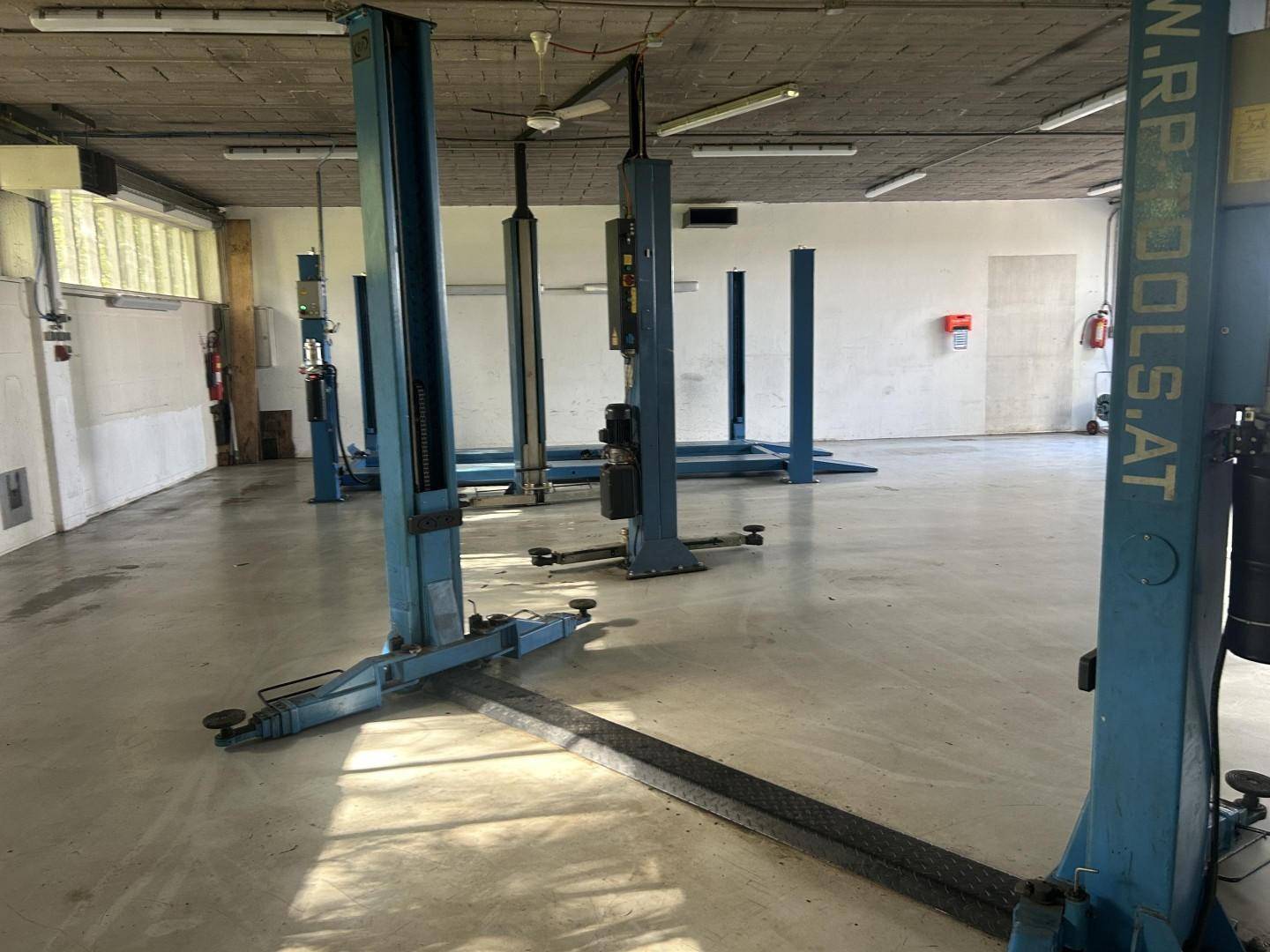 Innenansicht einer geräumigen Werkstatt mit mehreren Hebebühnen und Betonboden, gut beleuchtet.