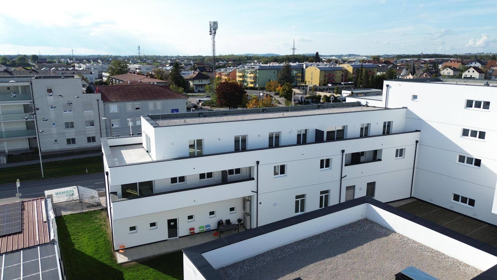 Luftaufnahme eines modernen Wohngebäudes mit Flachdächern, Balkonen und Blick auf die Umgebung.
