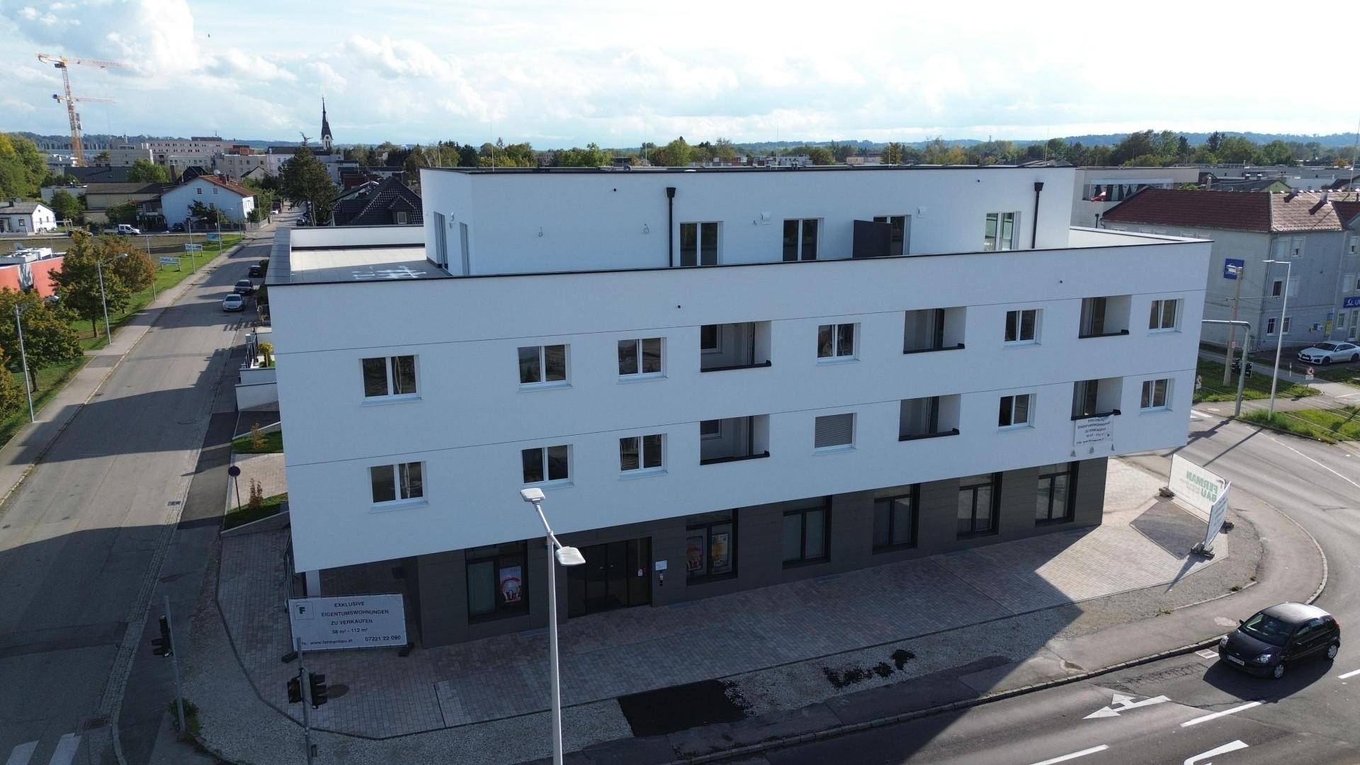 Luftaufnahme eines modernen Wohnkomplexes mit weißer Fassade, Flachdächern und umliegender Bebauung.