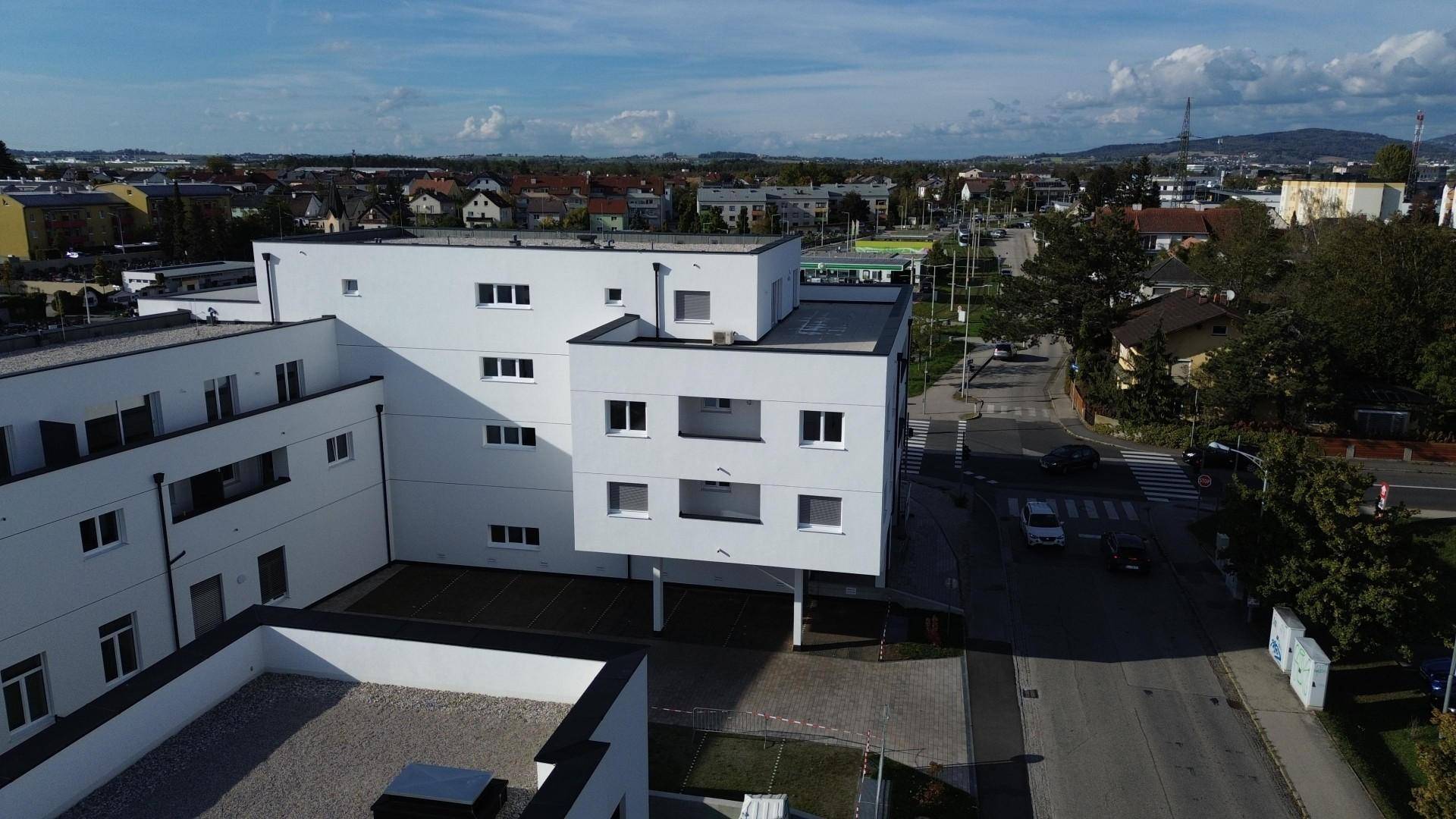 Luftaufnahme eines modernen Wohnkomplexes mit weißer Fassade, Flachdächern und umliegender städtischer Landschaft.
