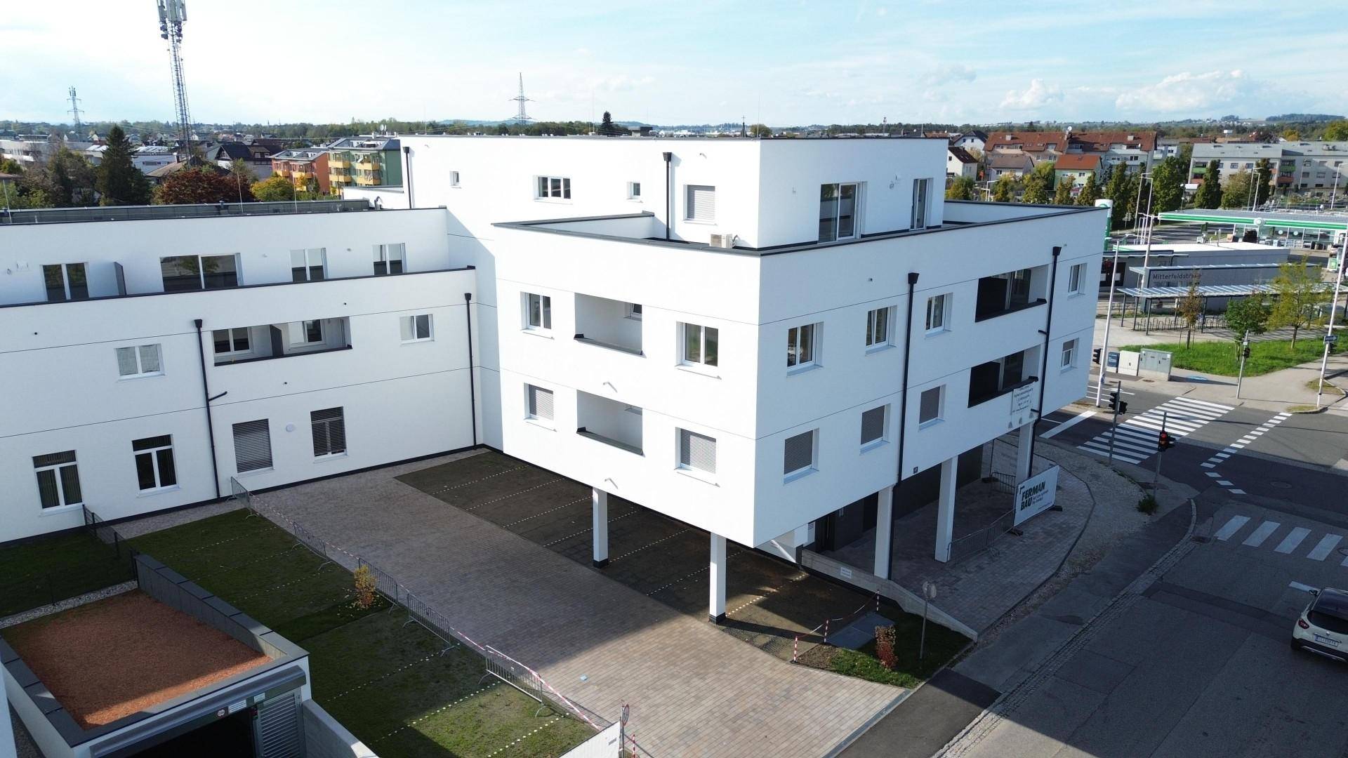 Luftaufnahme eines modernen Wohngebäudes mit Flachdächern, Parkplätzen und angrenzender städtischer Umgebung.
