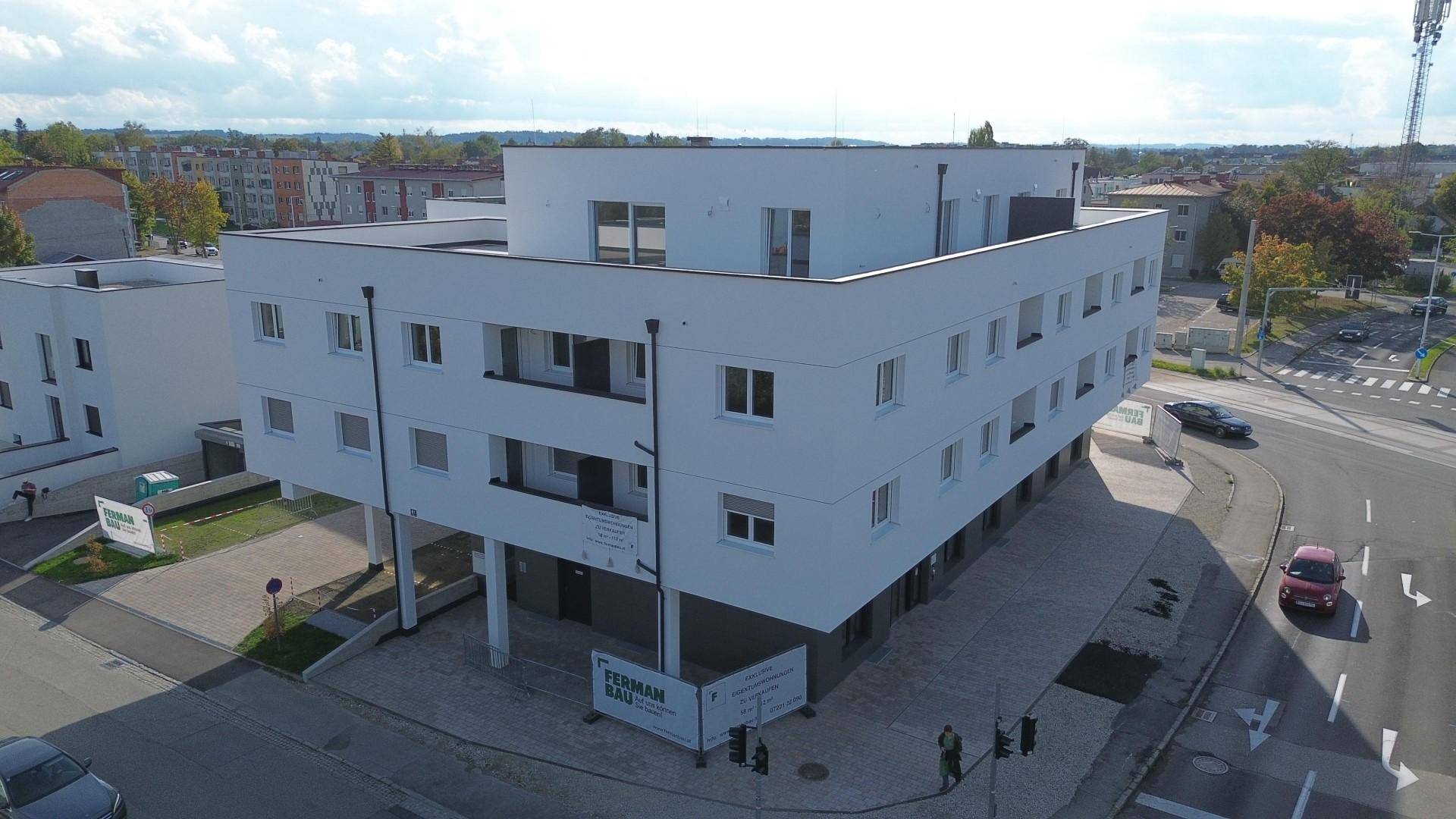 Luftaufnahme eines modernen Wohnkomplexes mit weißer Fassade, Flachdächern und umliegender Infrastruktur.