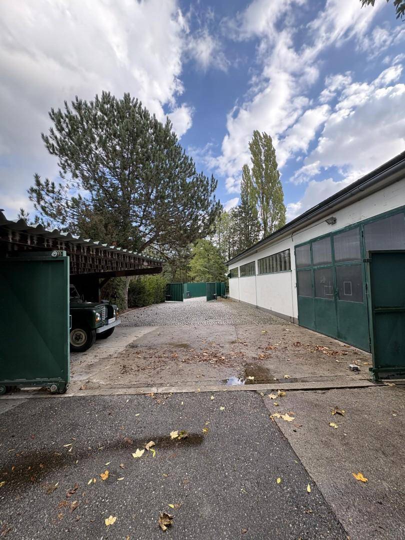 Außenbereich einer Gewerbeimmobilie mit Zufahrt, Parkplatz und angrenzendem Gebäude unter blauem Himmel.