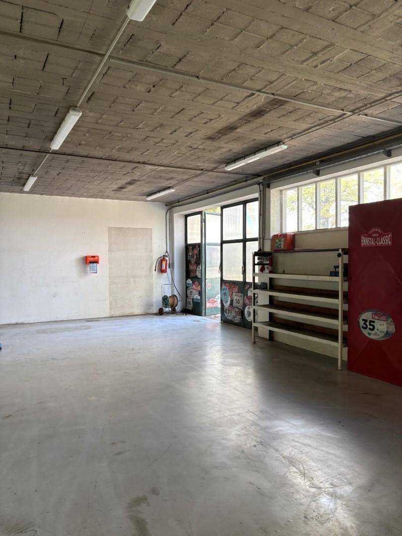 Geräumiger Werkstattbereich mit Betonboden, Regalen und einem offenen Eingangsbereich, hell beleuchtet.