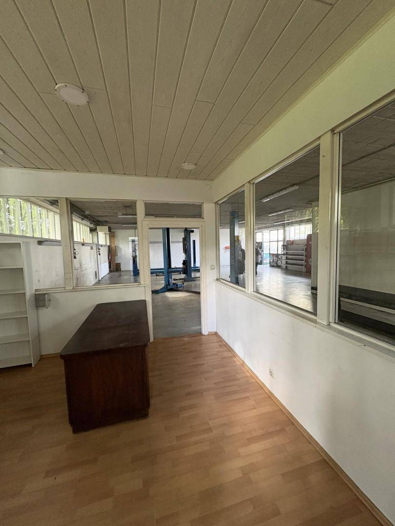 Büro mit Holzboden, Schreibtisch und großen Fenstern, die viel Tageslicht hereinlassen.