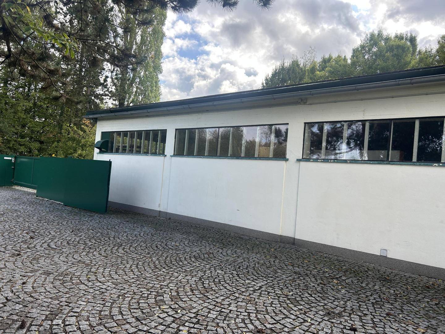 Seitenansicht des Gebäudes mit langen Fensterreihen und einem gepflasterten Bereich davor.