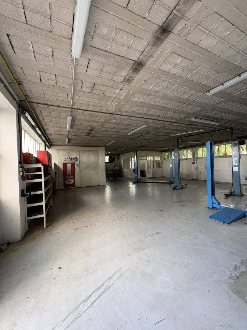 Großer Werkstattraum mit Betonboden, mehreren Hebebühnen und Fenstern für natürliche Belichtung.