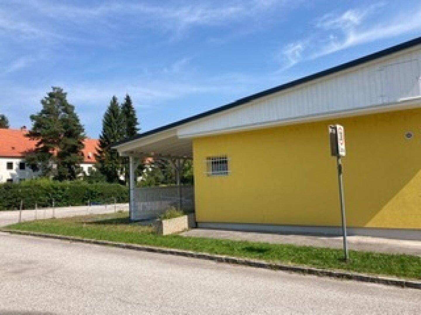 Seitenansicht eines gelben Gebäudes mit einem überdachten Bereich und einem kleinen Fenster mit Gitter.