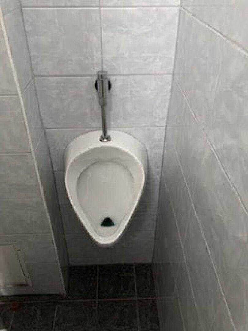 Sauberes Badezimmer mit Urinal und hellen Fliesen an den Wänden, funktional und gepflegt.