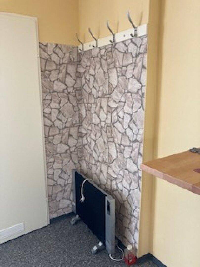 Kleiner Bereich mit Steinwand-Tapete und Kleiderhaken, daneben ein Heizkörper.