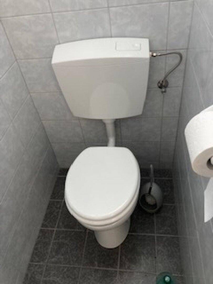 Kompakte Toilette mit grauen Fliesen an Wänden und Boden sowie einem Stand-WC.