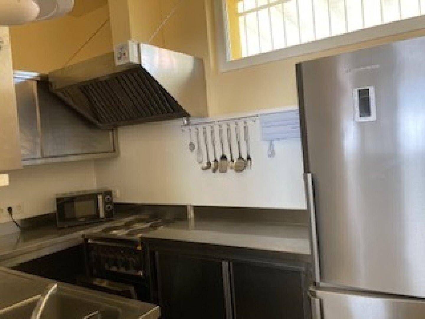 Professionelle Küche mit großem Kühlschrank, Dunstabzugshaube und Kochfeld, ideal für die Gastronomie.