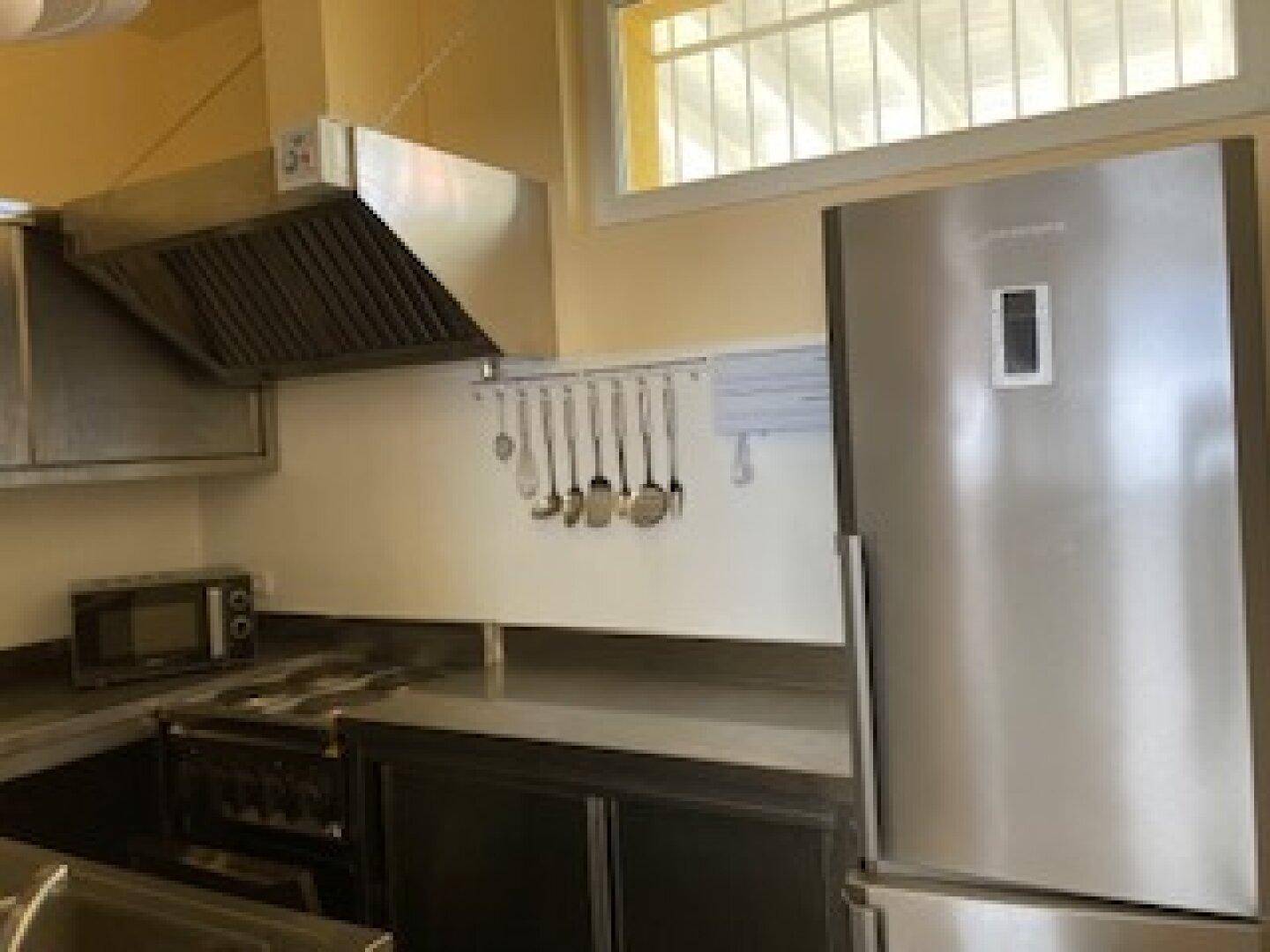 Professionelle Küche mit großem Kühlschrank, Dunstabzugshaube und Kochfeld, ideal für die Gastronomie.