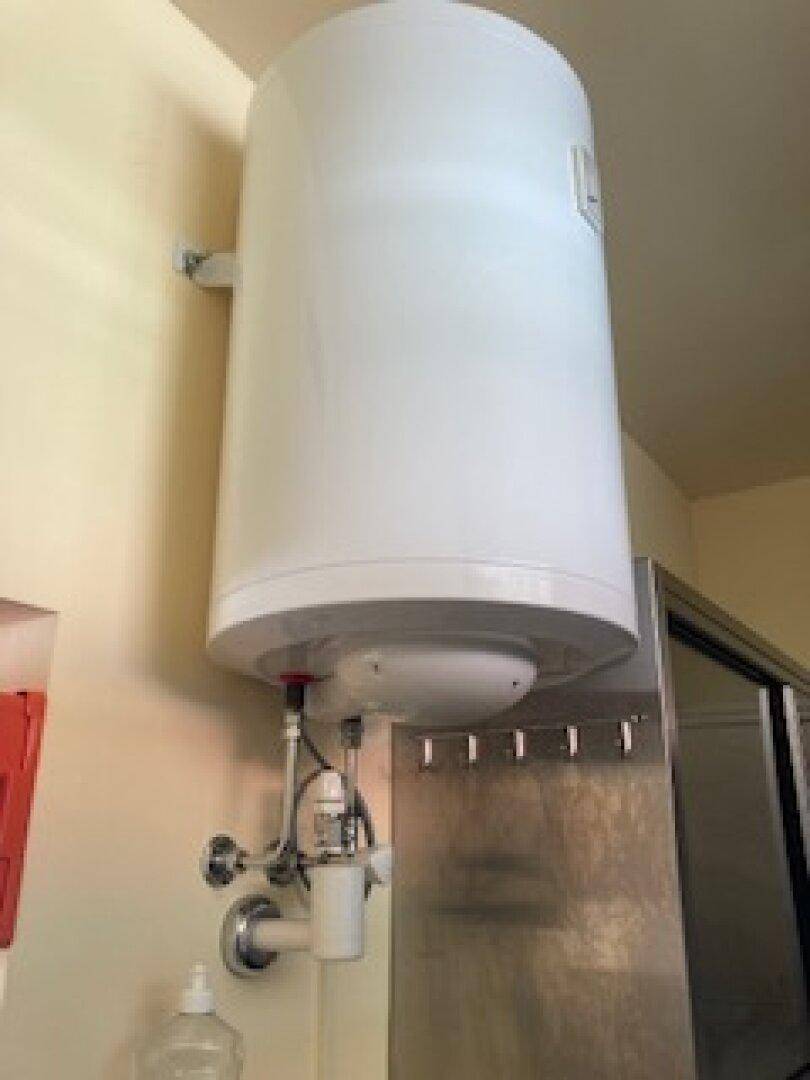 Wandmontierter Warmwasserbereiter in einem funktionalen Raum, daneben Edelstahlschränke.