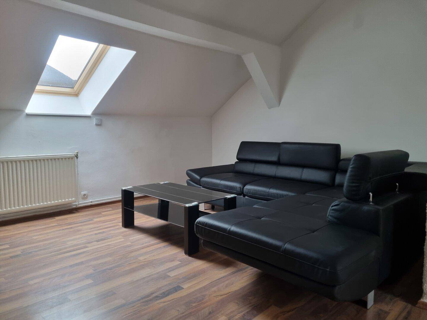 Gemütliches Wohnzimmer mit schwarzem Sofa, Couchtisch und viel Tageslicht durch das Dachfenster.