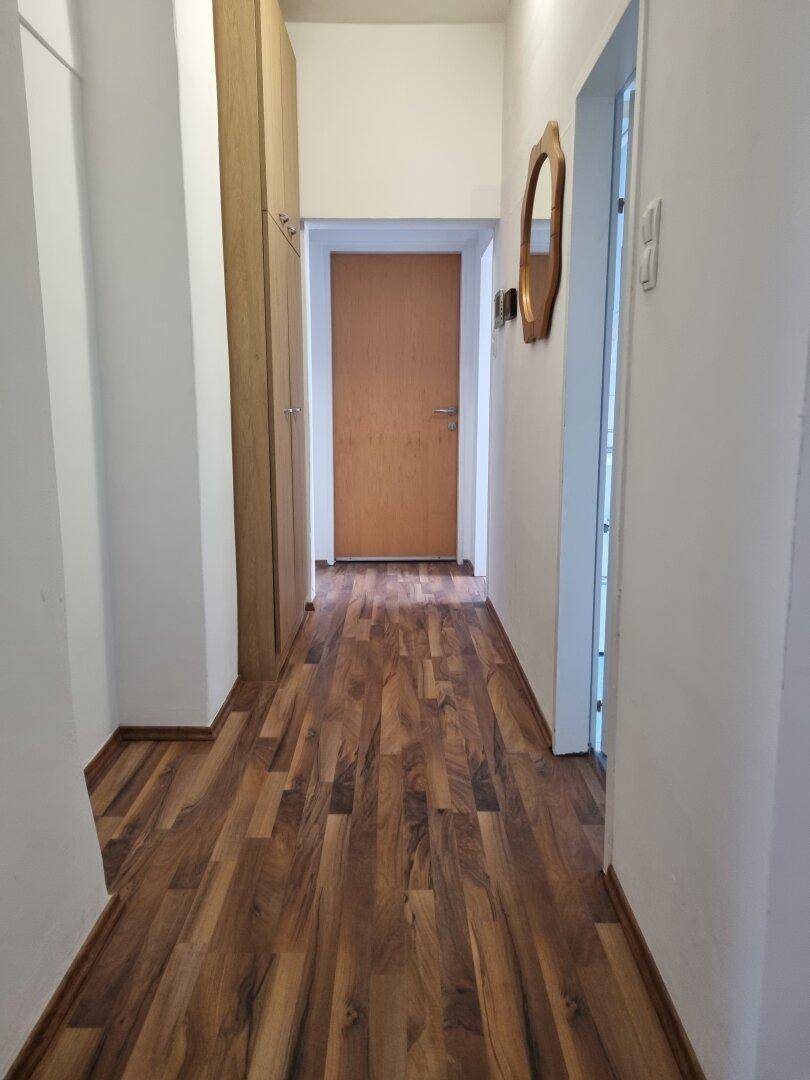 Langer Flur mit Laminatboden, Einbauschränken und einem Spiegel an der Wand.
