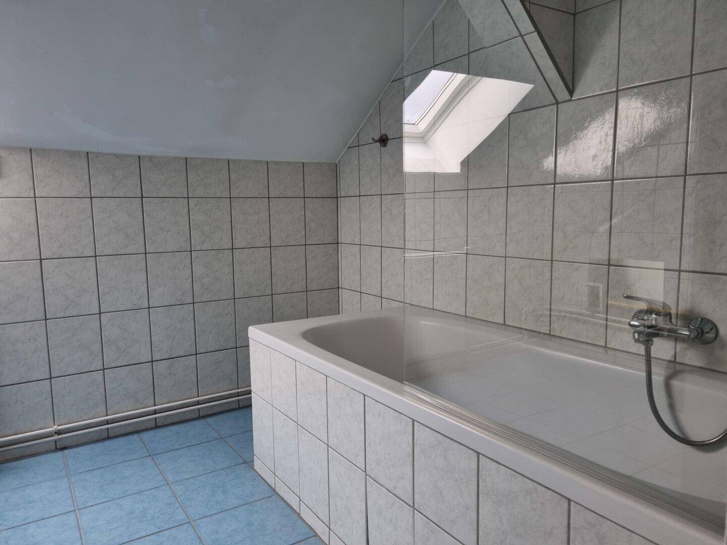 Badezimmer mit eingebauter Badewanne, hellen Fliesen und einem Dachfenster für Tageslicht.