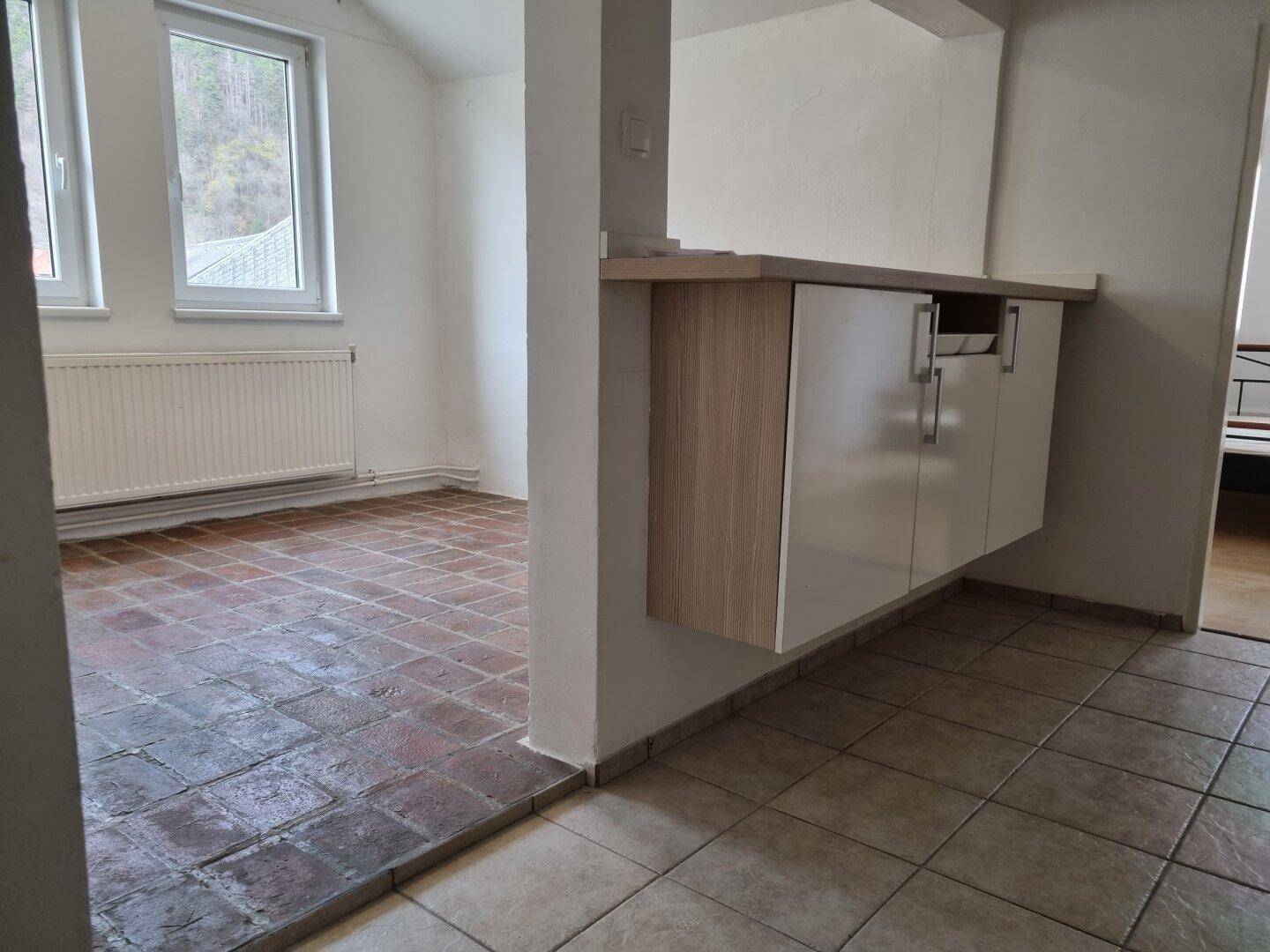 Übergangsbereich zwischen gefliestem Flur und einem Raum mit Terrakotta-Boden und grüner Aussicht.
