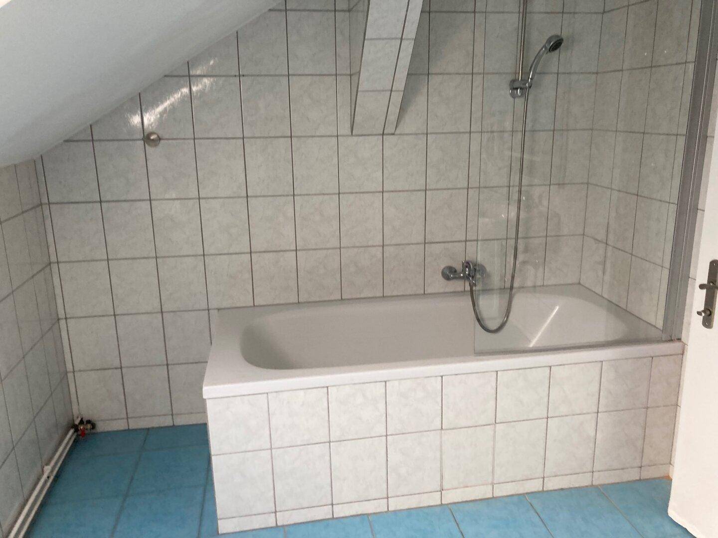 Badezimmer mit Badewanne, Duschvorrichtung, Fliesenwänden und schräger Decke.