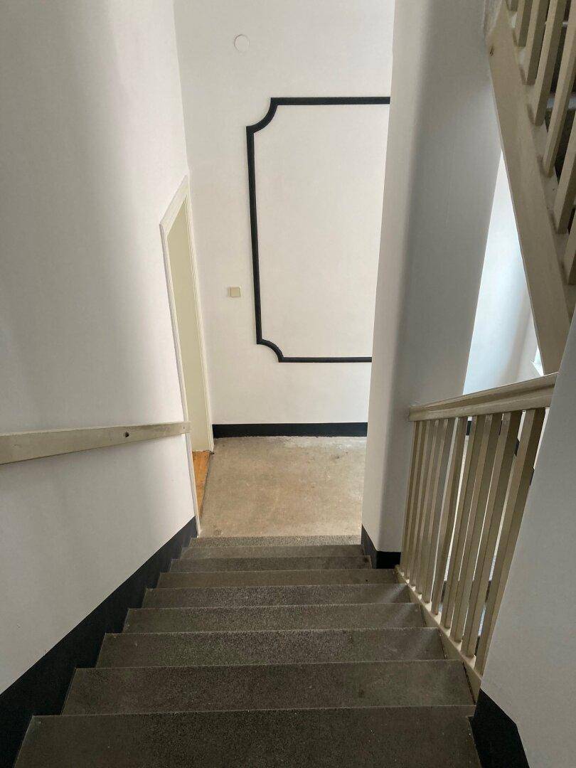 Treppenhaus mit Steinstufen, Holzgeländer und dekorativen schwarzen Akzenten an den Wänden.