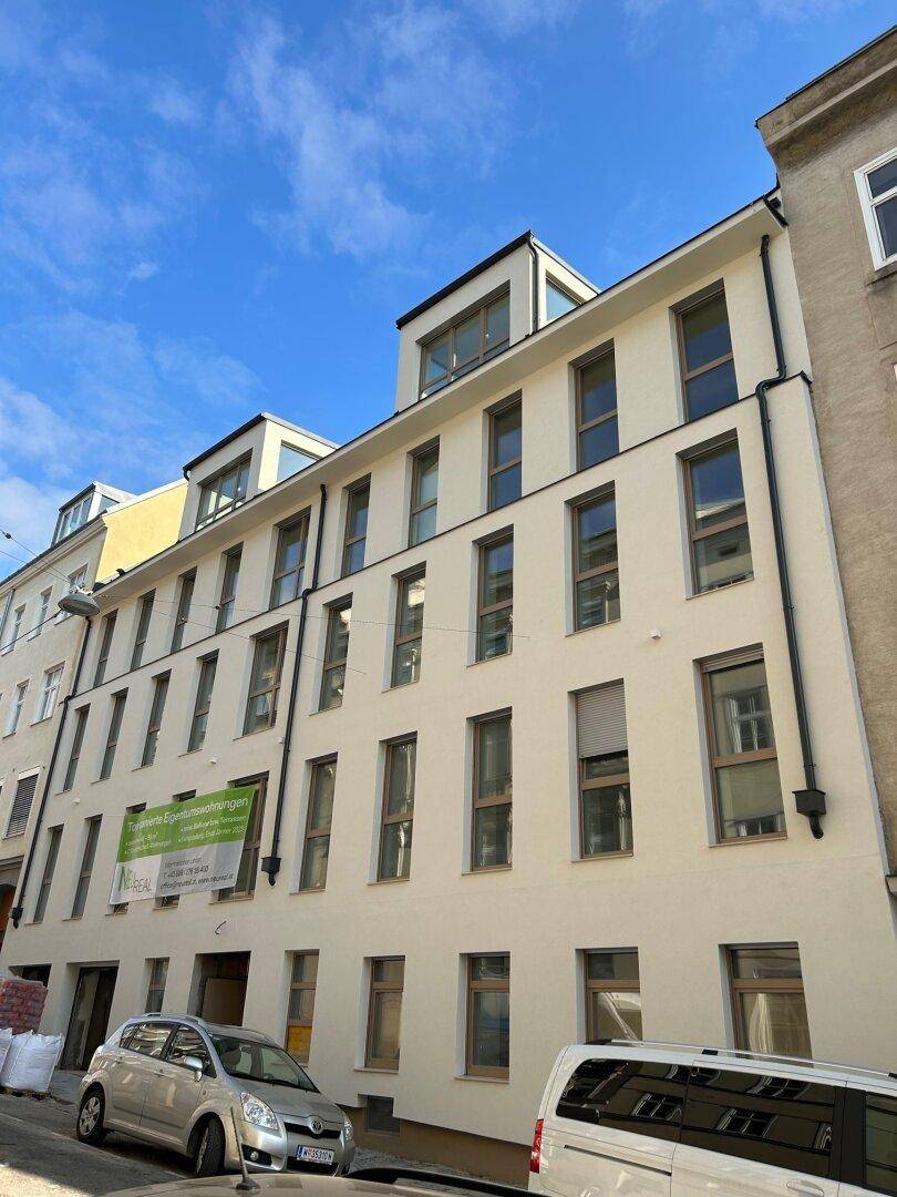 Modernes Mehrfamilienhaus mit heller Fassade, vielen Fenstern und Dachgauben unter blauem Himmel.