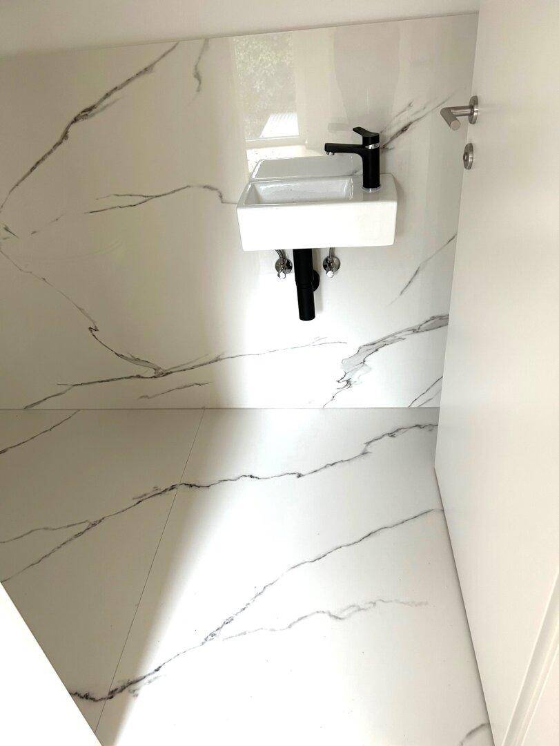 Modernes Waschbecken mit schwarzem Wasserhahn in einem Raum mit Marmoroptik-Fliesen und minimalistischem Design.