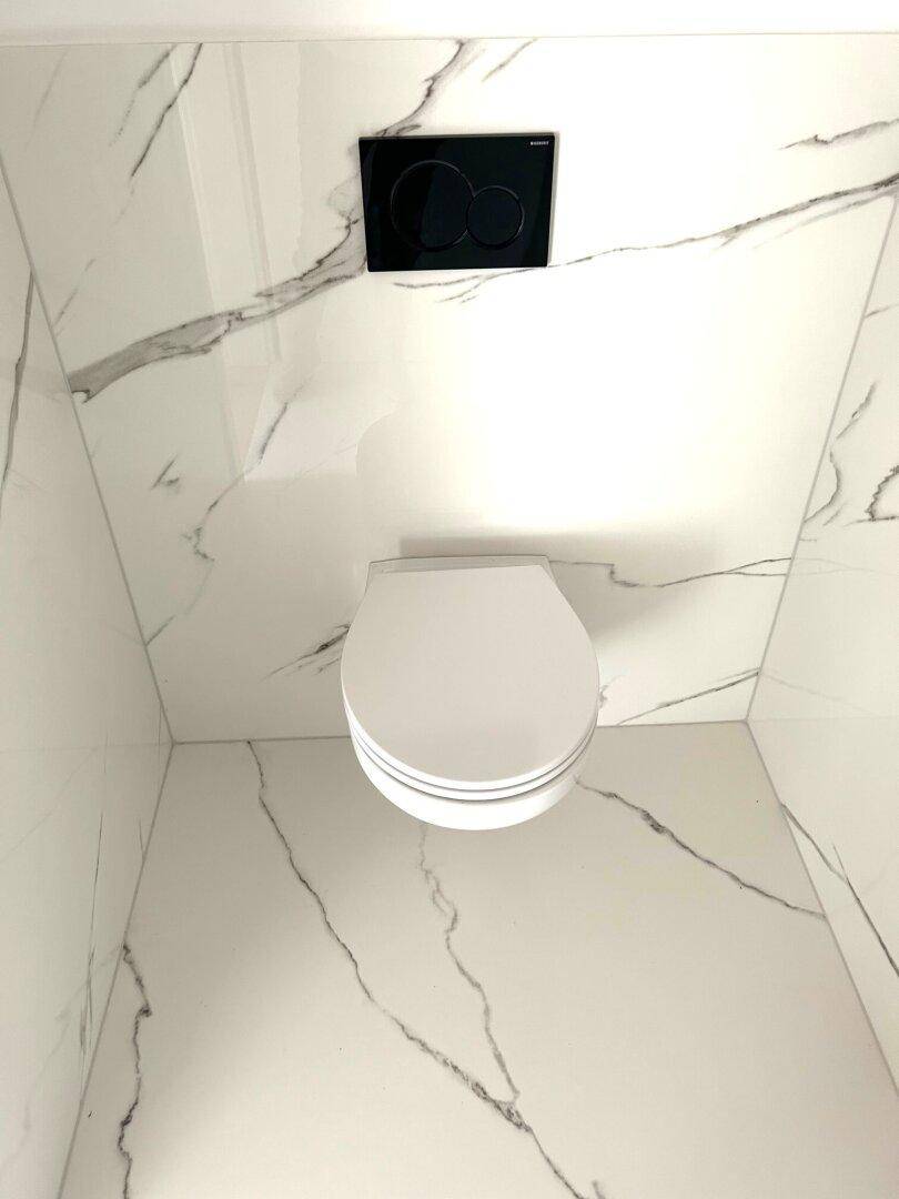 Wandhängendes WC mit schwarzer Spülplatte in einem modern gefliesten Raum mit Marmoroptik und sauberer Ästhetik.