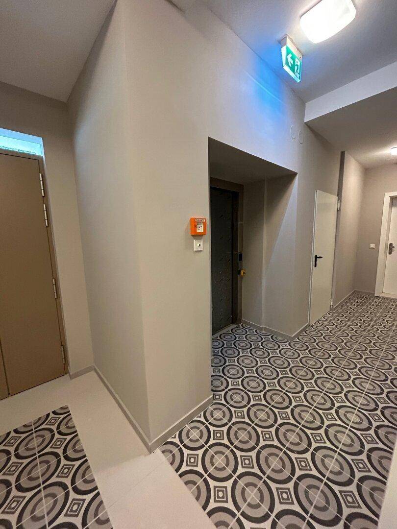 Flur mit gemusterten Bodenfliesen und Zugang zu einem modernen Aufzug, in einem gepflegten Zustand.