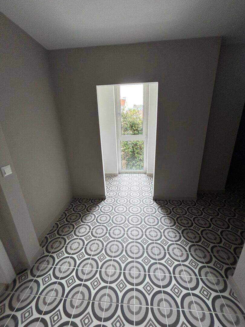 Raum mit gemusterten Bodenfliesen und einem hohen Fenster mit Blick ins Grüne, ideal für ein Büro.