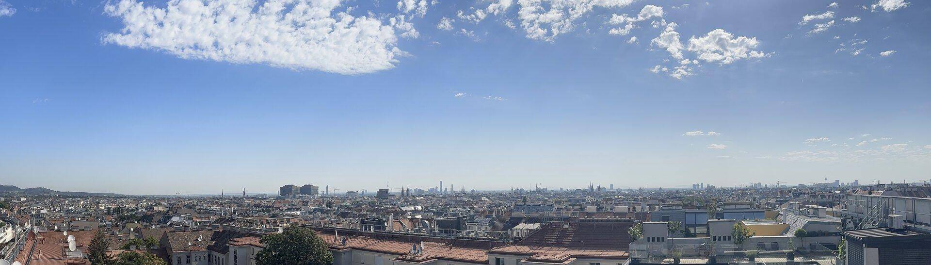 Panoramablick über die Stadt mit zahlreichen Gebäuden und einem weiten Horizont unter blauem Himmel.