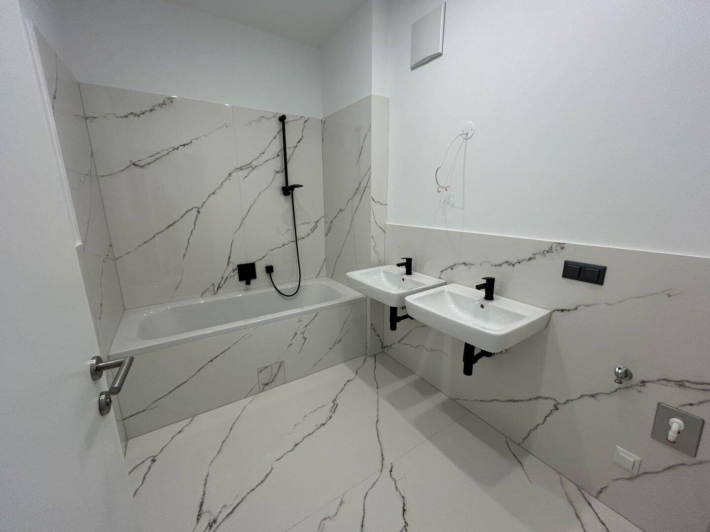 Modernes Badezimmer mit eleganten weißen Fliesen in Marmoroptik, schwarzen Armaturen, Badewanne und Doppelwaschbecken.
